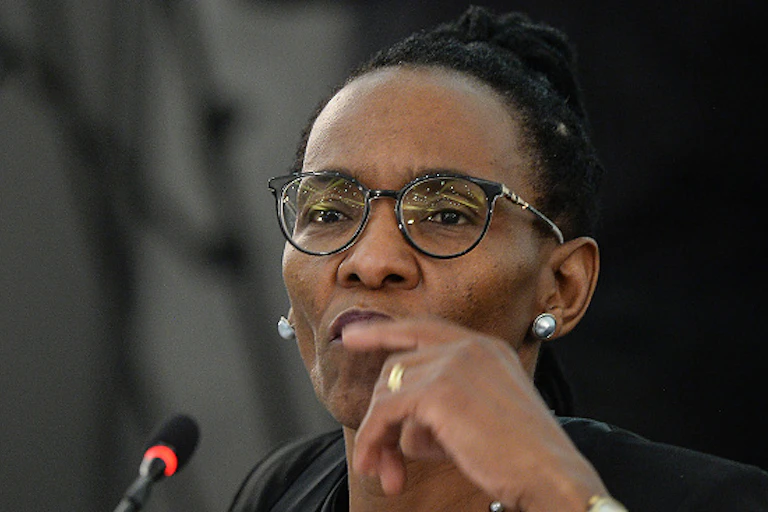 A black woman wearing reading glasses stares attentively