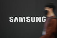 A man in a mask walks by a Samsung sign.