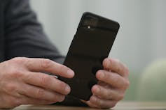 A man's hard hands are holding a black smartphone.