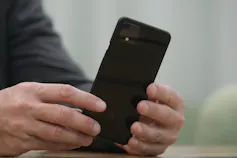 A man's hards hold a black smartphone.