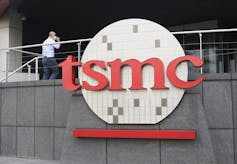 A man in a mask walks into a building with a TSMC logo on the front of it.