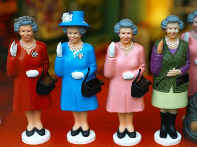 Four figurines of a waving and smiling Queen Elizabeth II in different outfits