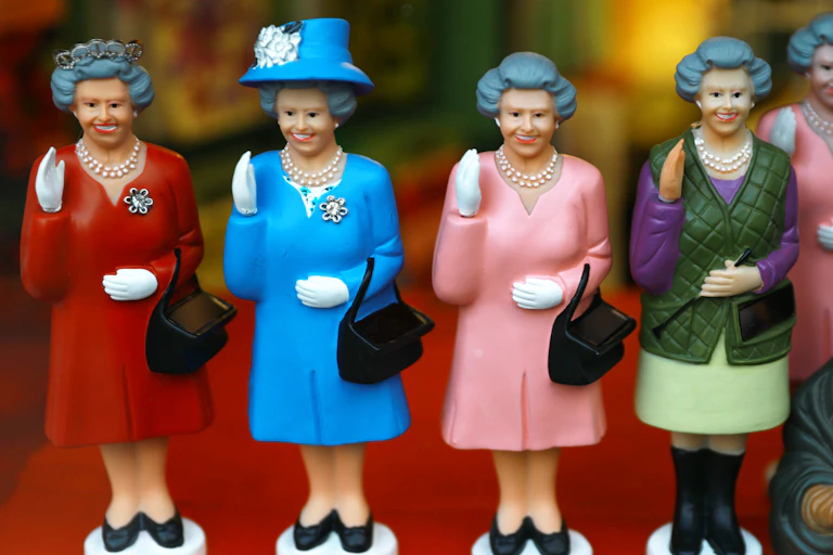 Four figurines of a waving and smiling Queen Elizabeth II in different outfits