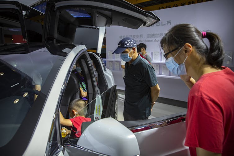 People warning face masks look at a Tesla.