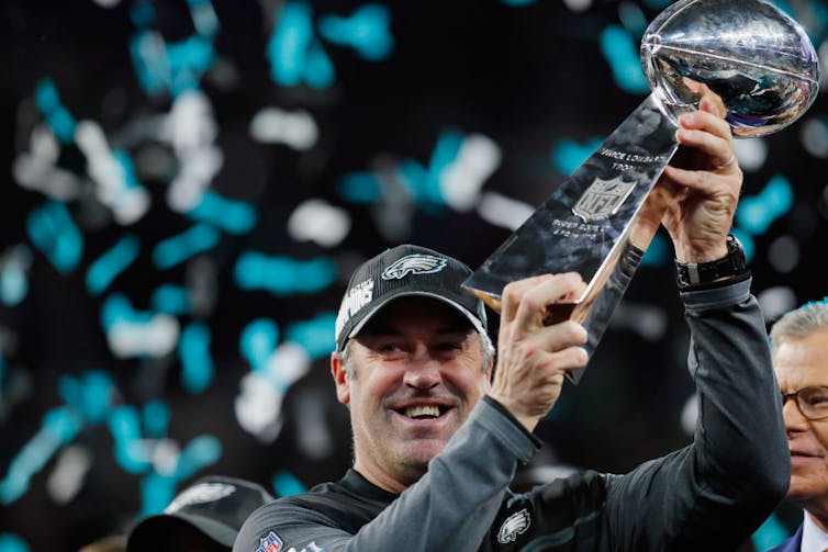 Man surrounded by confetti holds trophy.