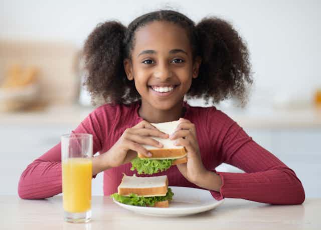 Smiling girl eating a sandwich with a glass of orange juice