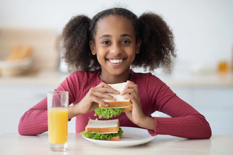Smiling girl eating a sandwich with a glass of orange juice