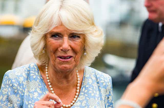 Close up photo of Camilla, Duchess of Cornwall wearing pearls and a blue floral top