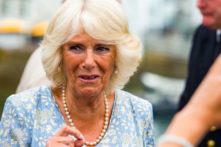 Close up photo of Camilla, Duchess of Cornwall wearing pearls and a blue floral top