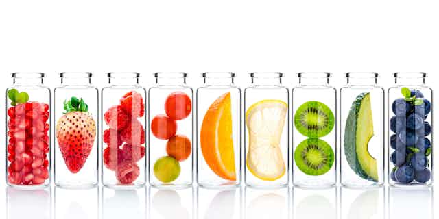 Glass bottles containing a variety of fruit against a white background