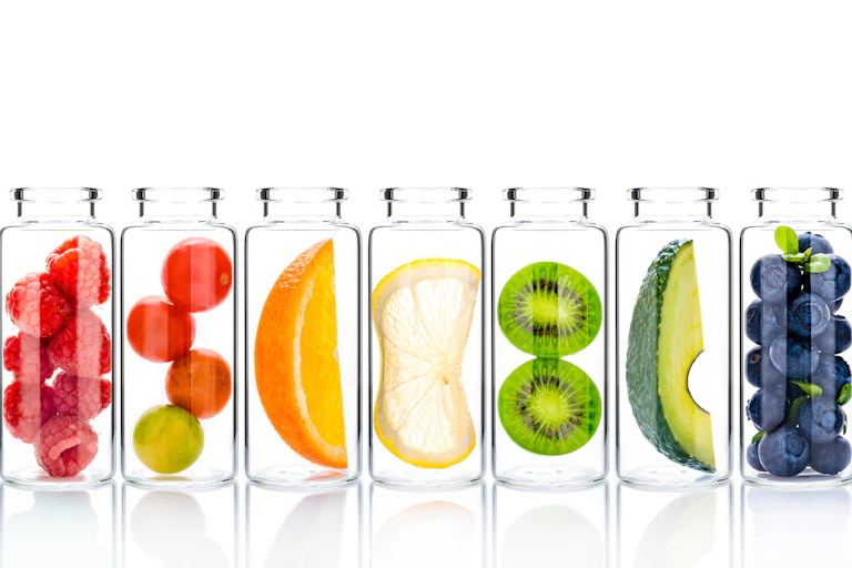Glass bottles containing a variety of fruit against a white background