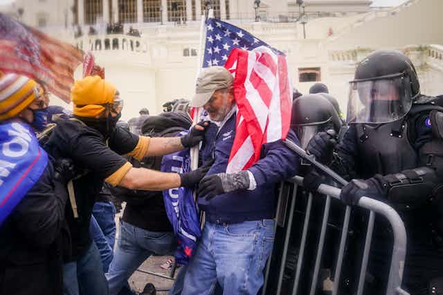 A person wearing protective gear grapples with another person, in front of police barricades