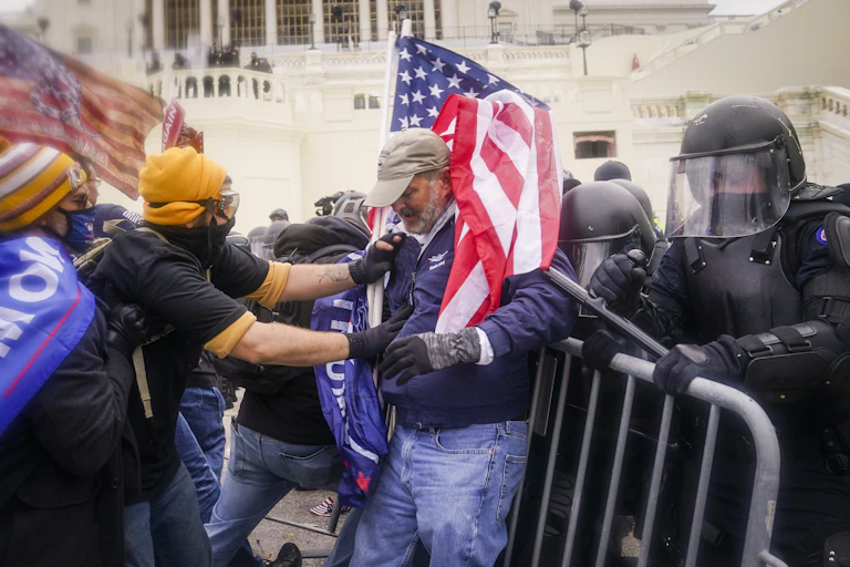A person wearing protective gear grapples with another person, in front of police barricades