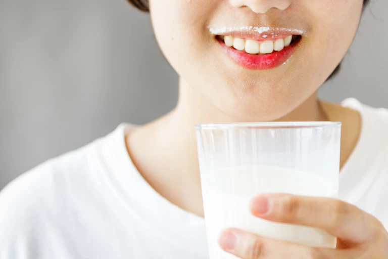 Asian girl smiles while holding a glass of milk.