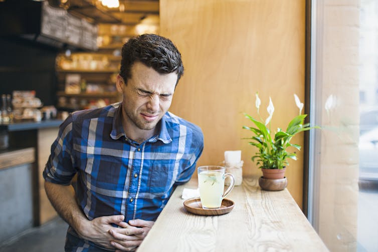 Man holds his stomach after drinking a milky coffee.