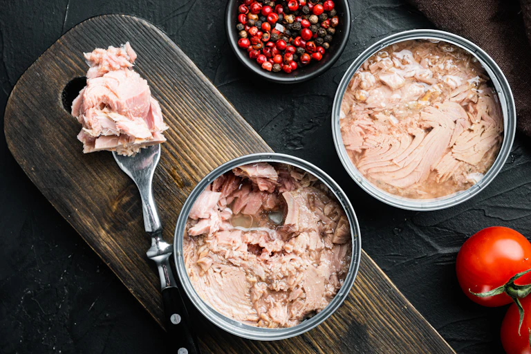Two cans of tuna lie open on a chopping board.