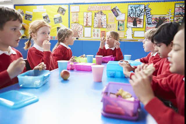 Schoolchildren eating food from their lunchboxes as they sit around a table