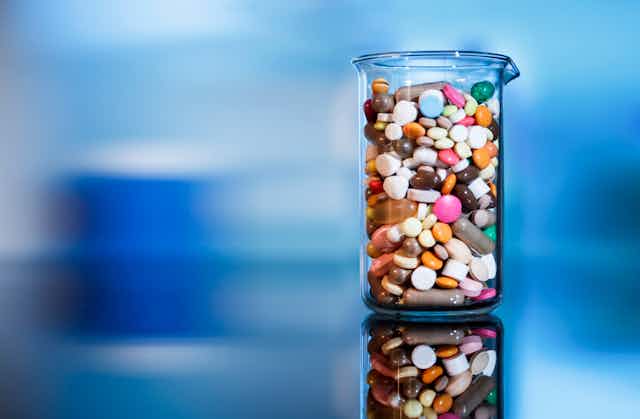 A glass beaker filled with assorted sizes, shapes and colors of pills.