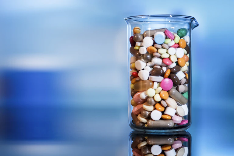 A glass beaker filled with assorted sizes, shapes and colors of pills.