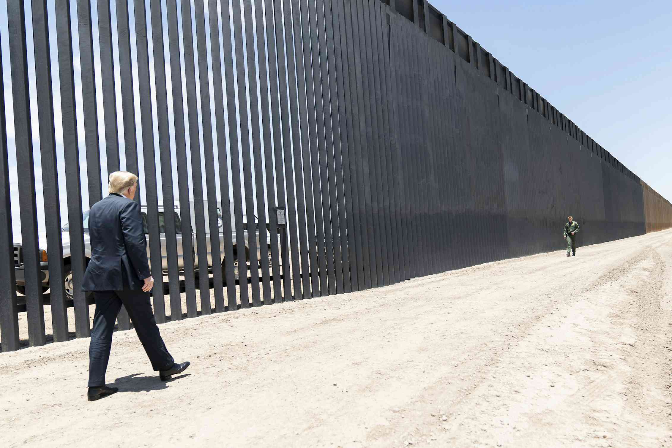 Man in suit walks along tall wall.