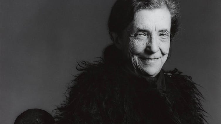 Older woman dressed in black, smiling mischievously.