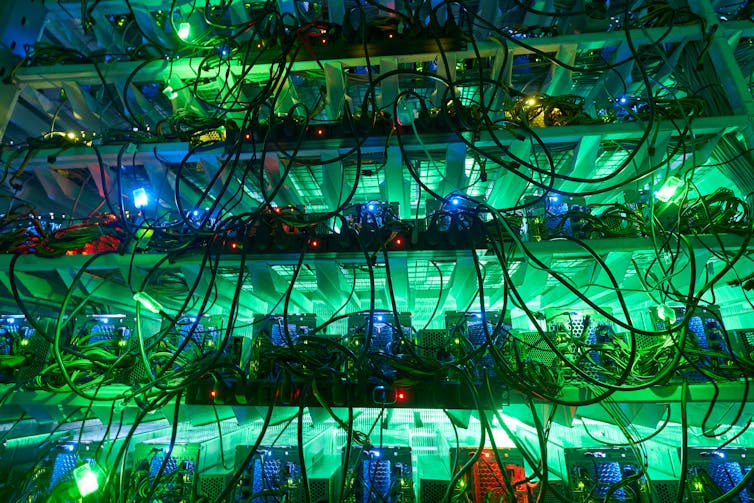 Shelves of computer servers strewn with cables and lit by green and blue lights.