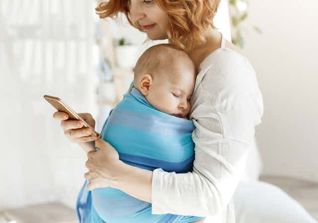 A mother holding her baby while on her phone