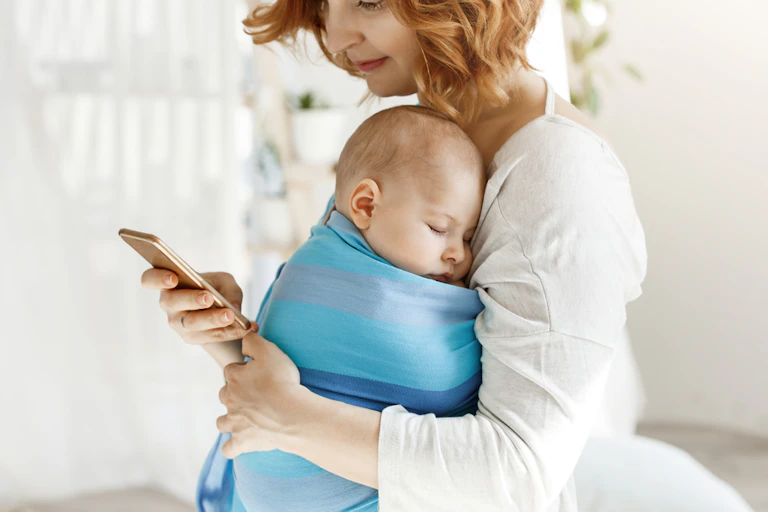 A mother holding her baby while on her phone