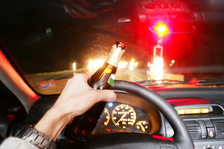 Persona conduciendo con una botella en la mano.