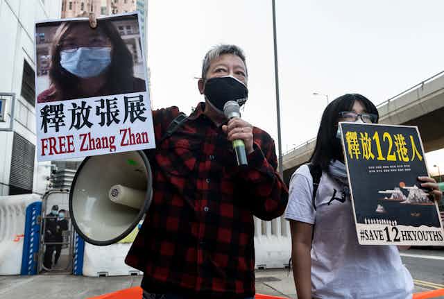 Hong Kong man and woman wearing masks protest with loudhailer and posters the detention of journalist Zhang Zhan.