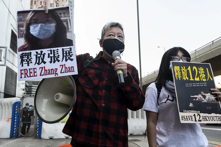 Hong Kong man and woman wearing masks protest with loudhailer and posters the detention of journalist Zhang Zhan.