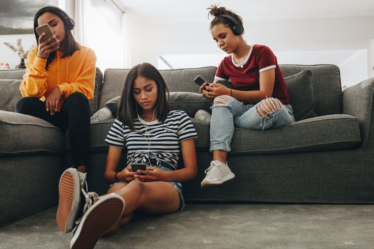 Three teenage girls sitting on a couch looking at their phones