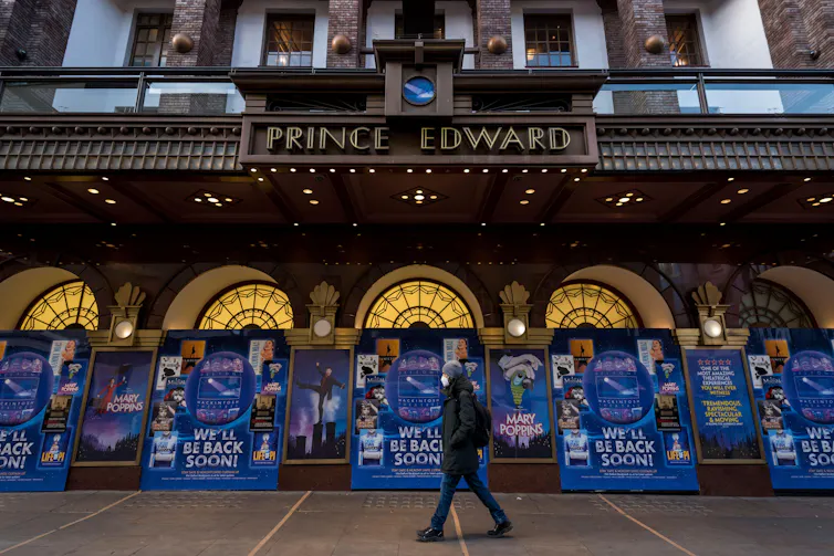 Man walks past a theatre, outside of which are signs reading 'We'll be back soon'