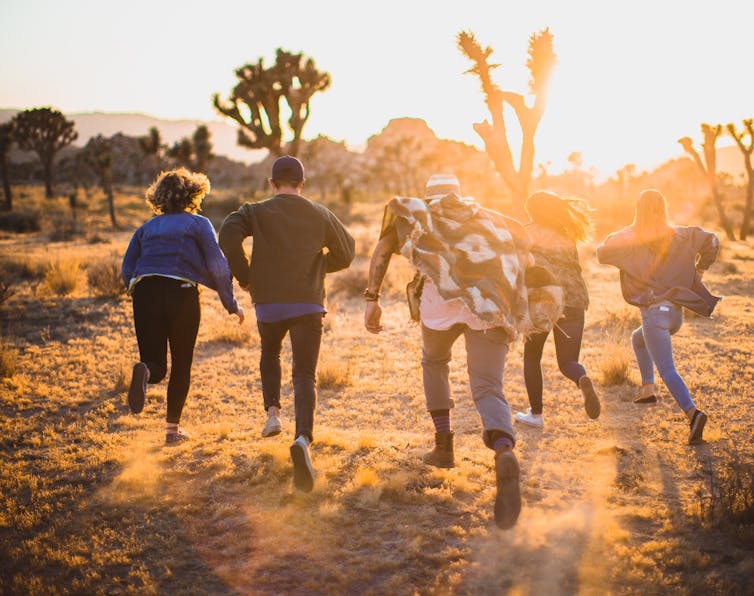People run into the sunlight in a desert setting.