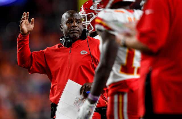 Man with headphones and red shirt raises hand.