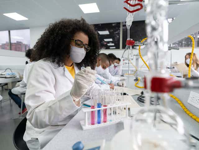 A Black woman works with test tubes in a science lab.