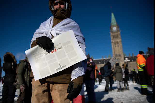 a man stands outside Parliament holding a copy of the CANADIAN CHARTER OF RIGHTS AND FREEDOMS