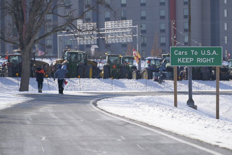 tractors and other vehicles block a road next to a sign reading CARS TO U.S.A. KEEP RIGHT