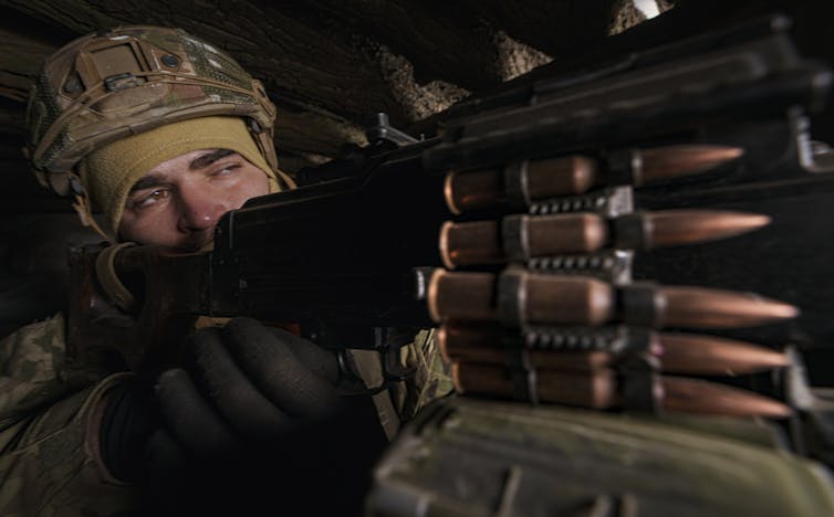 A man in battle fatigues and a helmet holds a heavy machine gun.
