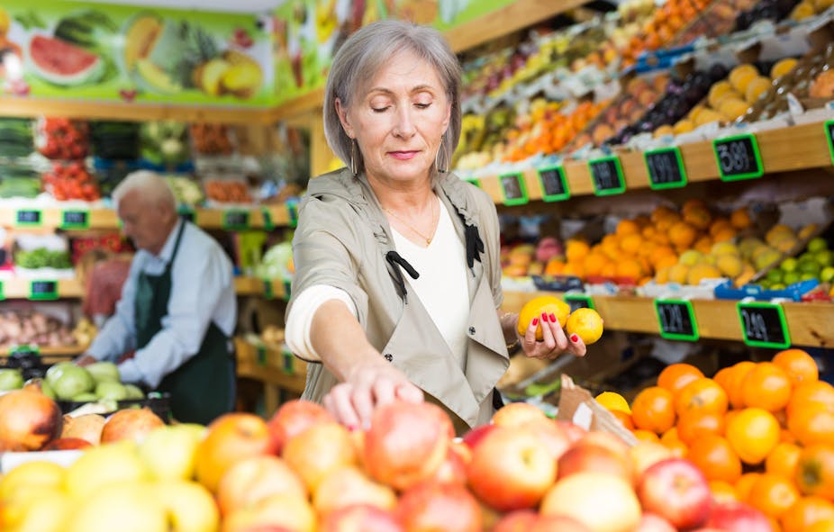 An elderly woman shops for fruit in a supermarket.