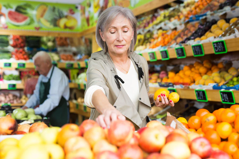 An elderly woman shops for fruit in a supermarket.