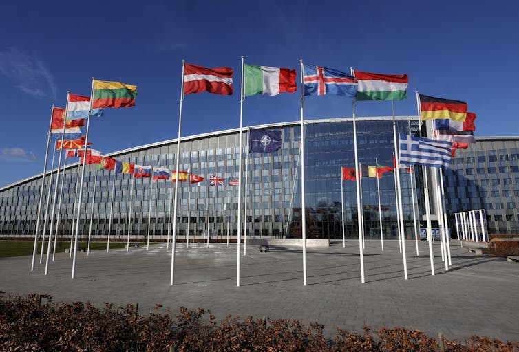 A gleaming glass building is seen with a circle of flags and flagpoles in front of it.