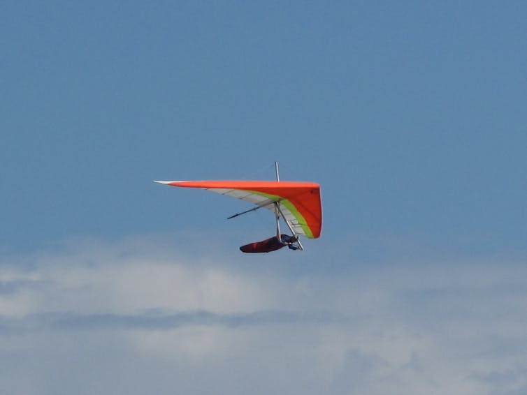A person flying with a red triangular hang glider.