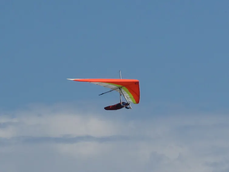 A person flying with a red triangular hang glider.