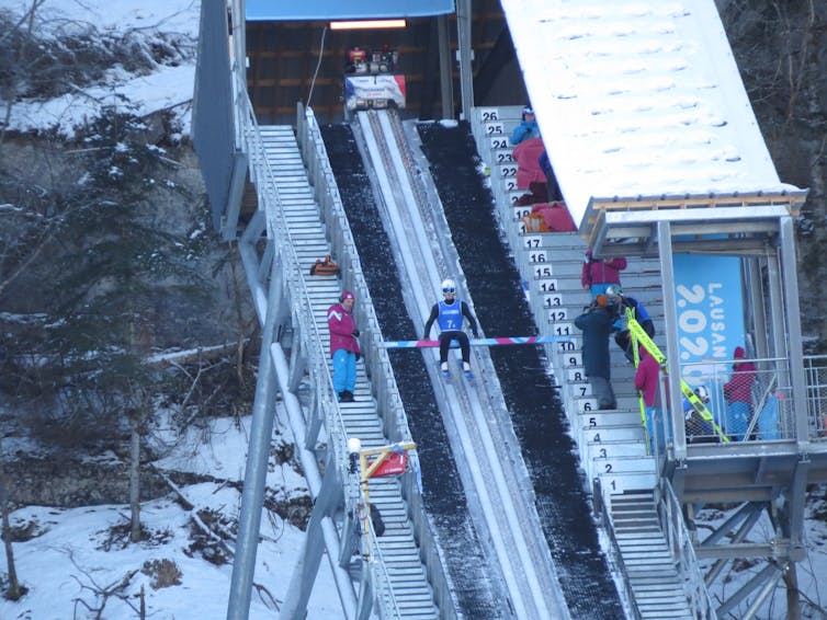 A ski jumper sitting on the start bench showing how it can be moved.