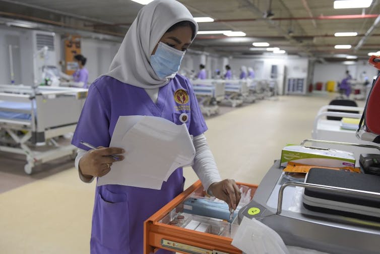 Health care worker wearing a headscarf looking through a medical supply drawer in an ICU.