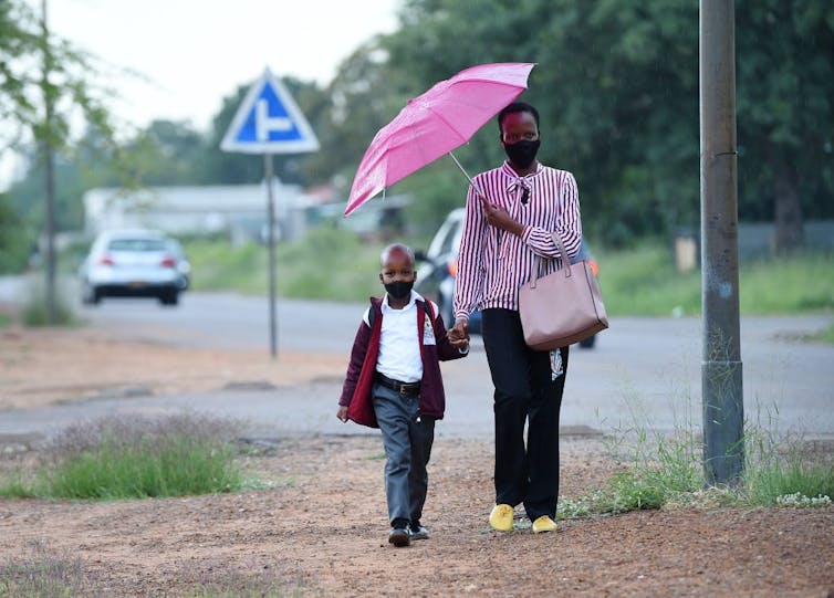 Parent and child walking together holding hands under an umbrella.
