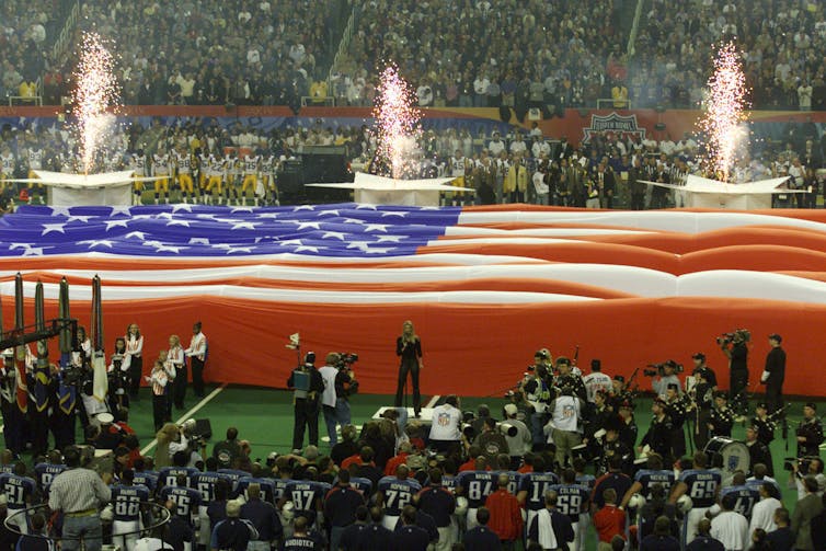 An enormous American flag covers the football field during the playing of the national anthem.
