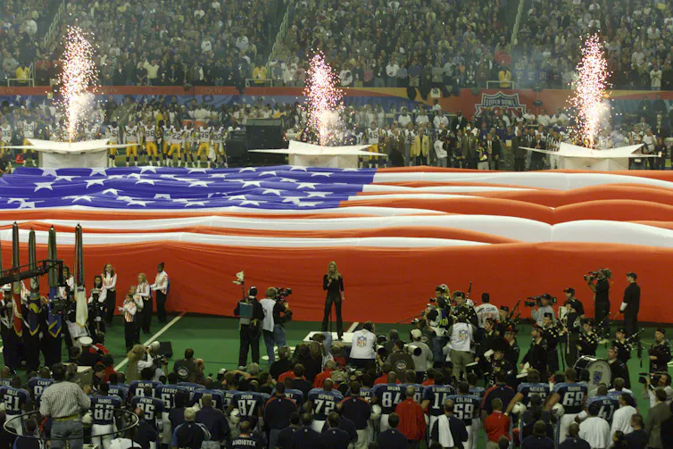 An enormous American flag covers the football field during the playing of the national anthem.
