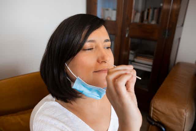 Woman taking own nasal swab with face mask around neck